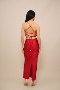 Rode satijnen jurk met een aansluitende rok, open rug, gekruiste bandjes en een zijslit. Bevat een stippenpatroon en minimale hardware accenten.