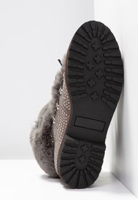 Botte dotée d'une tige texturée grise avec des clous décoratifs, doublure en fourrure et une semelle en caoutchouc noir robuste avec un motif de crantage pour l'adhérence.