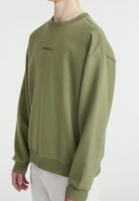 Zielona bluza z miękkiego materiału, z okrągłym dekoltem, spadniętymi ramionami i ściągaczami na rękawach. Na piersi znajduje się subtelne logo.