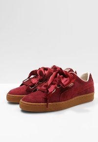 Baskets en velours côtelé rouge avec de grands lacets en satin, bout arrondi et semelle en caoutchouc beige. Détails du logo sur le côté et accents intérieurs crème visibles.