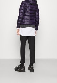 Paars donzen jack met capuchon, doorgestikt ontwerp en grijze gebreide zoom, gecombineerd met zwarte broek met wijde pijpen en zwarte sneakers.