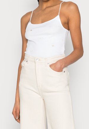 White camisole with adjustable straps featuring a subtle pattern. Paired with high-waisted, textured cream wide-leg pants with a pocket.