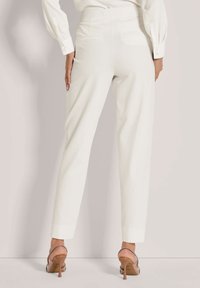 Witte op maat gemaakte broek met een aansluitende tailleband, rechte pijpen en achterzakken, gecombineerd met lichtroze hakken met een dunne hak.