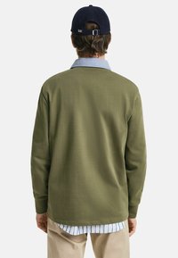 Olive green pullover with long sleeves, a light blue collar, and a layered light blue and white striped undershirt visible at the hem.
