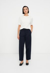 Λευκή πλεκτή μπλούζα με κοντά μανίκια και υφασμένο σχέδιο, σε συνδυασμό με μπλε σκούρο παντελόνι φαρδιάς γραμμής. Η εμφάνιση ολοκληρώνεται με μαύρα μπαλαρίνια.