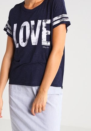 Persona che indossa una maglietta blu navy con la scritta "LOVE" in grandi lettere bianche e una gonna a righe blu chiaro e bianco.