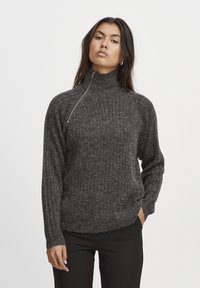 Rebrasta, temno siva pulover z visokim ovratnikom in pol-zadrgo, narejena iz teksturirane pletenine. Dolgi rokavi z oprijetimi manšetami.