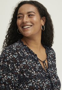 Kukkatrikoo, jossa tummansininen tausta ja valkoisia, sinisiä ja ruskeita kukkakuvioita. Aaltoreunaiset kaulus ja sidontadetali etuosassa.