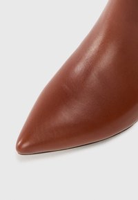 Chaussure en cuir marron à bout pointu avec une texture lisse, présentant une silhouette épurée et un design minimaliste, idéale pour les tenues formelles.