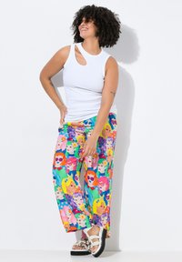Světlé široké kalhoty s různobarevným potiskem ilustrovaných obličejů s různými účesy. Vrchní část je bílý přiléhavý top s výřezem.