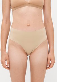 Woman wearing beige seamless high-waist underwear and matching bra, standing against a plain white background, front view.