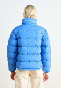 Niebieska kurtka puchowa z wysokim kołnierzem, z pikowanym wzorem i elastycznymi mankietami. Logo "HELly Hansen" na kołnierzu.