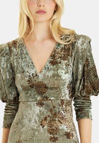 Samtkleid mit tiefem V-Ausschnitt, puffigen Ärmeln und brauner Blumenstickerei auf olivgrünem Hintergrund. Weicher Stoff und filigranes Design.