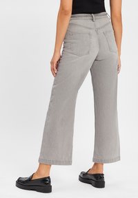 Szare szerokie dżinsy z wysokim stanem, z dwoma tylnymi kieszeniami i czystym wykończeniem. Modelka zestawia je z czarnymi butami na platformie.