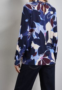Blusa a fiori blu con maniche lunghe, collo alto e dettaglio a chiave sul retro. Realizzata in tessuto leggero, con polsini arricciati.
