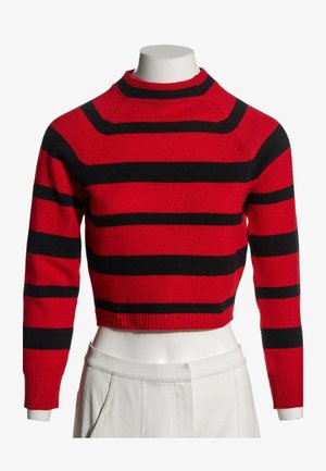 Suéter corto rojo con rayas horizontales negras expuesto en un maniquí torso que lleva pantalones blancos.
