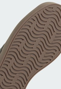 Gumowa podeszwa buta z falistym wzorem, posiadająca fakturowaną powierzchnię w jasnobrązowym kolorze. Solidna konstrukcja z wyraźnymi rowkami zapewniającymi przyczepność.