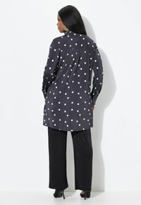 Zwarte blouse met stippenpatroon, met een vloeiende ontwerp, lange mouwen en een gebogen zoom, in combinatie met zwarte wijde broek en hakken.
