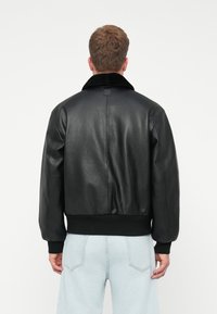 Fekete bőr bombázó dzseki plüss gallérral, bordázott mandzsettával és aljjal; sima textúrával és laza illeszkedésű dizájnnal rendelkezik.