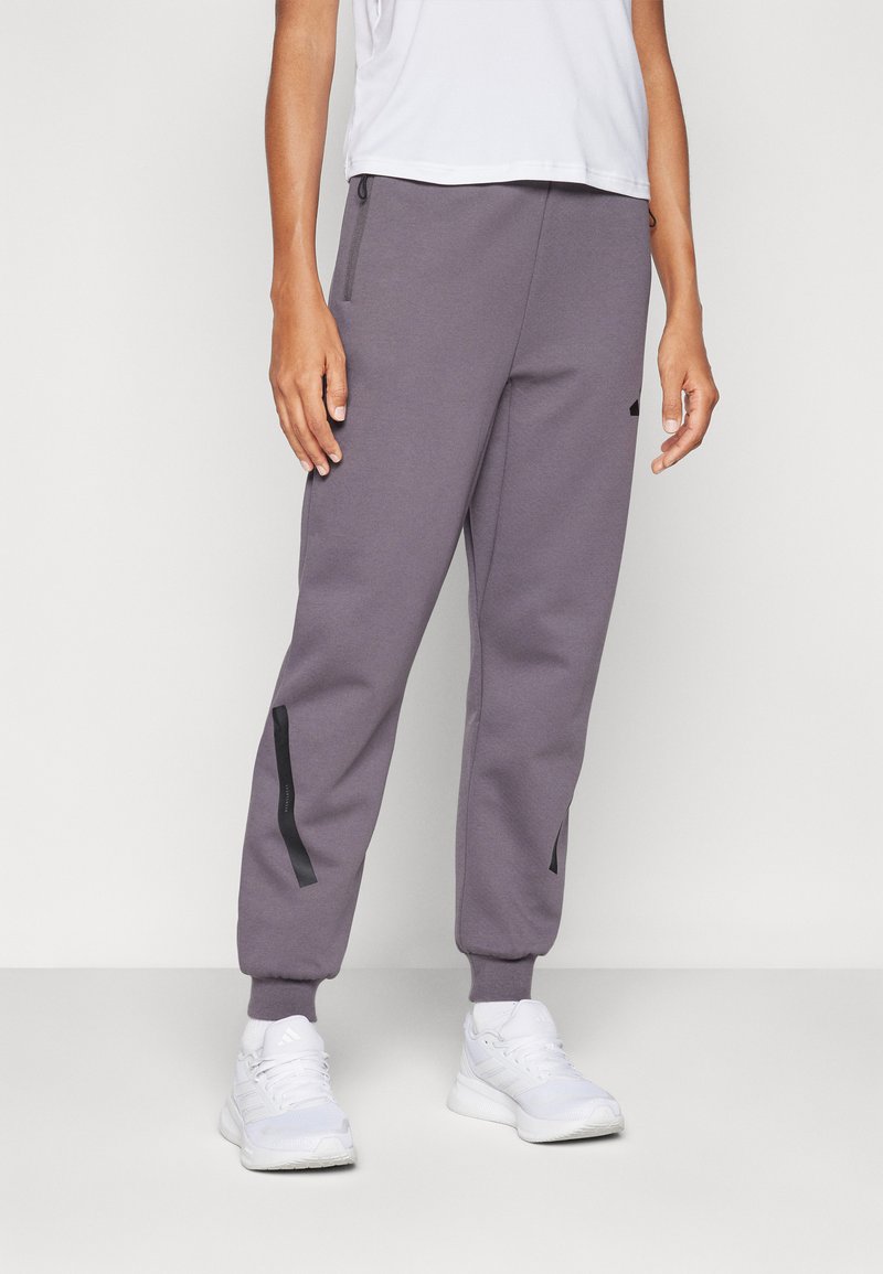 Grå joggebukser laget av mykt stoff, med sidelommer med glidelås og svarte detaljer. Tapered fit med ribbestrikkede mansjetter ved ankelen.