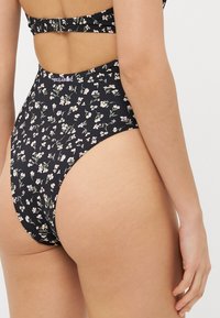 Schwarzes Badeanzug mit floralem Muster, mit hohem Beinausschnitt und ausgeschnittenem Rückendesign. Weicher, elastischer Stoff verbessert den Komfort und die Passform.