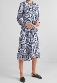 Langärmliges Hemdkleid im schwarz-weißen Schlangenprint, mit Kragen und Knopfleiste, kombiniert mit dunklen Slippern.