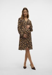 Vestido de estampado de leopardo con mangas largas y escote en V, ceñido debajo del busto. Combinado con pantuflas de tacón marrones, de textura suave, a la altura de la rodilla.