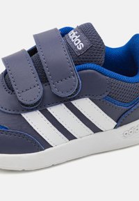 Mørkeblå sneakers med to borrelåser, hvite tre striper, teksturert stoff og gummisåle med Adidas-logo.
