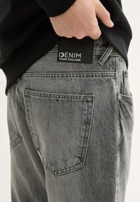 Szare dżinsy denimowe o teksturowanym wykończeniu, z tylnymi kieszeniami, czarną metką z napisem "DENIM TOM TAILOR" oraz przeszyciami.