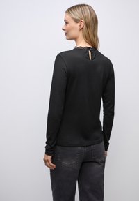 Schwarzes Langarmoberteil mit einem Spitzenbesatz am Kragen und einem Schlüssellochdetail auf der Rückseite. Weicher Stoff mit einer taillierten Passform.