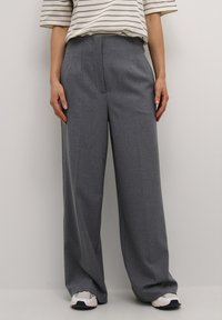 Grijze comfortabele wijde broek van gestructureerde stof, met voorplooien, zijzakken en een plat tailleband, gecombineerd met witte sneakers.