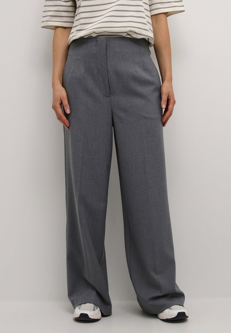 Grijze comfortabele wijde broek van gestructureerde stof, met voorplooien, zijzakken en een plat tailleband, gecombineerd met witte sneakers.