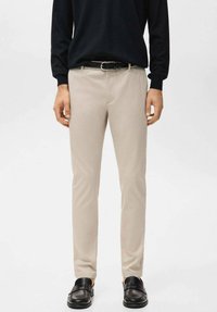 Pantaloni color beige chiaro con una vestibilità slim, realizzati in tessuto morbido. Presentano una cintura con fibbia in metallo argentato e sono abbinati a scarpe slip-on nere.