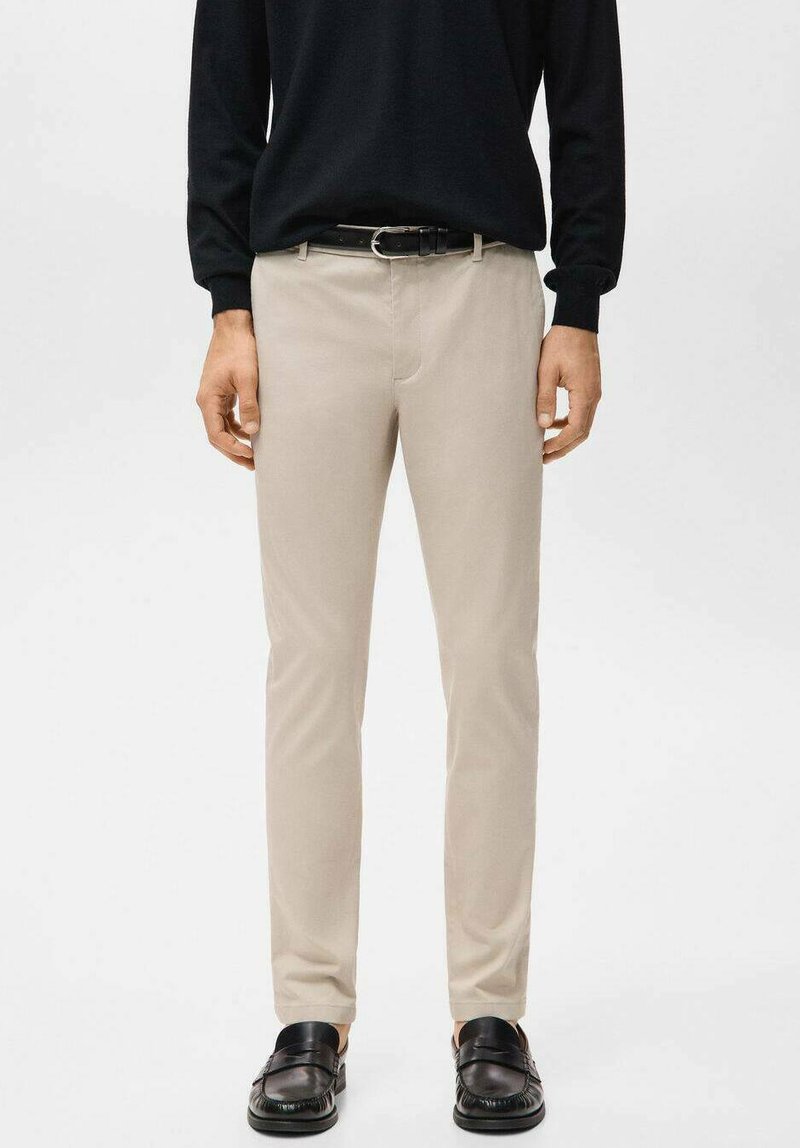 Pantaloni color beige chiaro con una vestibilità slim, realizzati in tessuto morbido. Presentano una cintura con fibbia in metallo argentato e sono abbinati a scarpe slip-on nere.