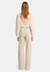 Beige wijde pantalon met hoge taille. Het bovenstuk heeft een diepe V-rug en lange mouwen, gemaakt van een lichtgewicht, zacht materiaal.