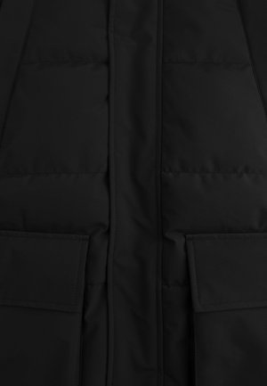 Zwart gequilt stoffen met een verticale naad in het midden en twee rechthoekige flapzakken nabij de onderkant.