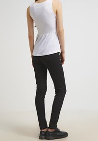 Top bianco senza maniche con orlo peplum, abbinato a jeans skinny neri e scarpe nere. Tessuto liscio, design aderente, dettagli minimi.