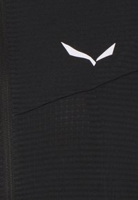 Svart träningslinne i texturerat tyg, med en triangel-formad vit logotyp på övre bröstområdet och en halv dragkedja.