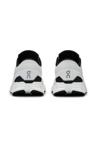 Baskets de sport blanches et noires avec une tige en mesh, un talon arrondi, une semelle texturée et un détail de logo sur le côté. Conçues pour le confort et la performance.