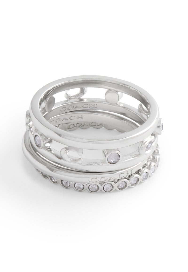 Anillos apilados de plata con varios diseños, que incluyen recortes circulares y piedras preciosas claras, con marca grabada en el interior de las bandas.