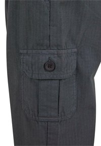 Bolsillo de tela gris oscuro con una solapa asegurada con un solo botón negro en una prenda, mostrando costuras y textura detalladas.
