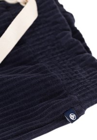 Marineblauwe gestructureerde stof met een geribbeld patroon, geaccentueerd door een crèmekleurige band en een klein logolabel aan de onderrand.