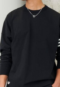 Černé tričko s dlouhým rukávem vyrobené z bavlny s kulatým výstřihem. Na levém rukávu má malé bílé logo a tři bílé pruhy.