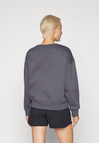 Sudadera gris de corte relajado, con cuello redondo y puños de canalé. La tela parece suave con un detalle de costura mínimo. Combinada con pantalones cortos negros.