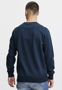Marineblauwe sweatshirt met ribgebreide boorden en zoom, ronde halslijn, gemaakt van textuurstof, toont de achteraanzicht, gecombineerd met lichtblauwe jeans.