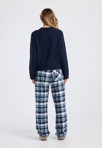 Navy knitted sweater with long sleeves paired with blue and white plaid flannel pants, featuring a pocket and relaxed fit.