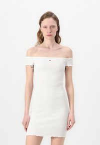 Valge õlgadelt kukkuv kleit, millel on smock-tekstuur, slim fit ja laineline äär. Rinnal on väike logo detail.