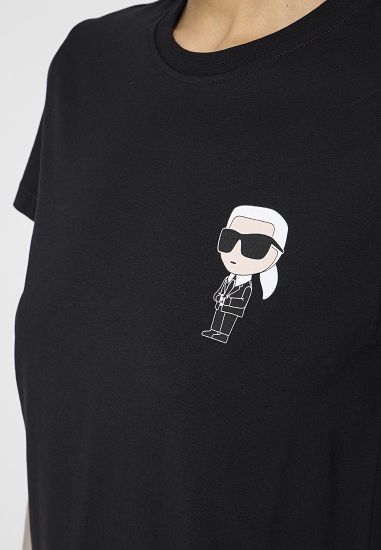 Schwarzes T-Shirt mit kurzen Ärmeln, das auf der linken Brustseite eine weiße Cartoonfigur mit Sonnenbrille und Anzug zeigt.