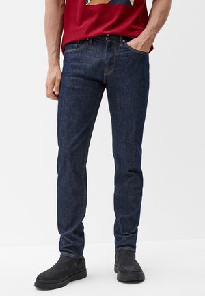 Donkerblauwe denim jeans met een slim fit, voorzien van vijf zakken en koperen stiksels, gedragen met zwarte suède enkellaarsjes.