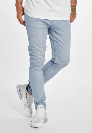 Vaqueros de corte slim en un tono azul claro, con una textura de mezclilla suave y detalles de costura simples, combinados con zapatillas deportivas blancas.
